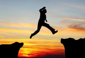 Silhouette of hiking man jumping over the mountains at sunset