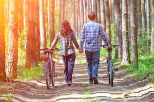 Young happy couple bicycles in the forest and holding hands